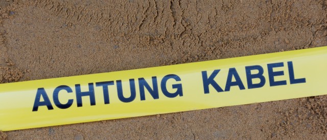 Gelbes Band auf Sand mit der Aufschrift Achtung Kabel